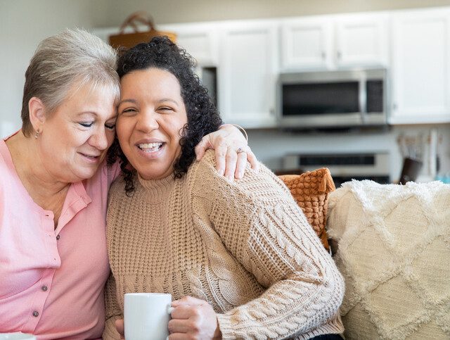 Senior woman spending time at home with her adult daughters and granddaughter. Women are drinking coffee and looking at family photographs.