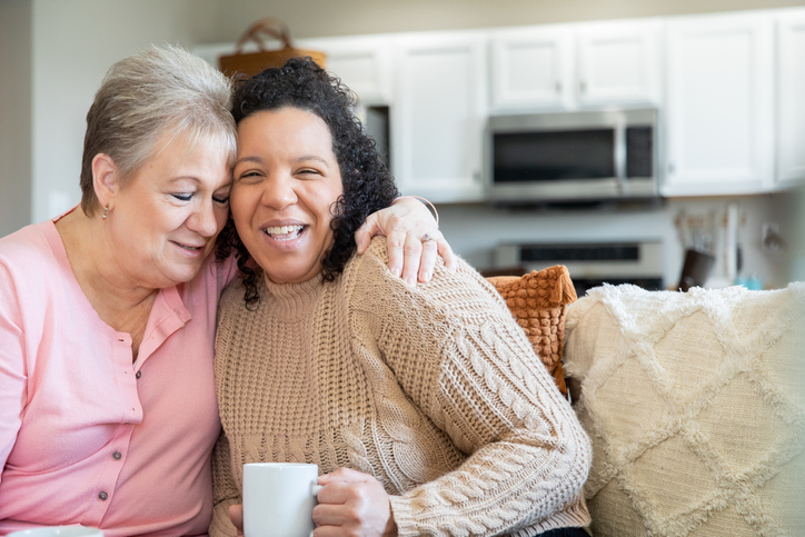 Senior woman spending time at home with her adult daughters and granddaughter. Women are drinking coffee and looking at family photographs.