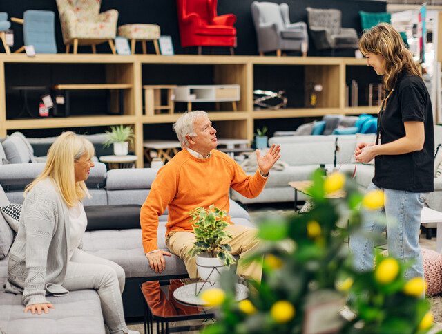 two seniors speaking with an interior design specialist at a furniture store.