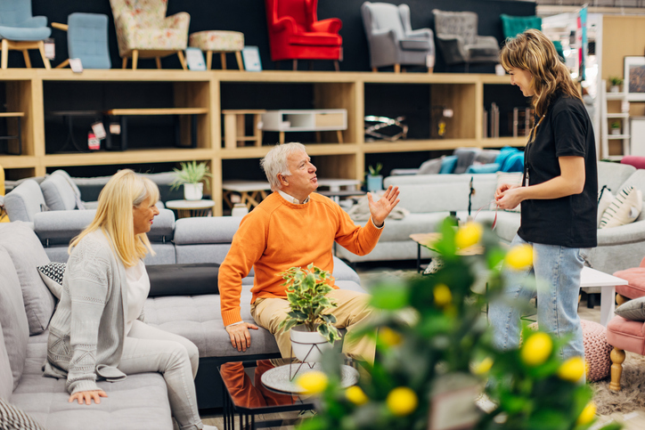 two seniors speaking with an interior design specialist at a furniture store.